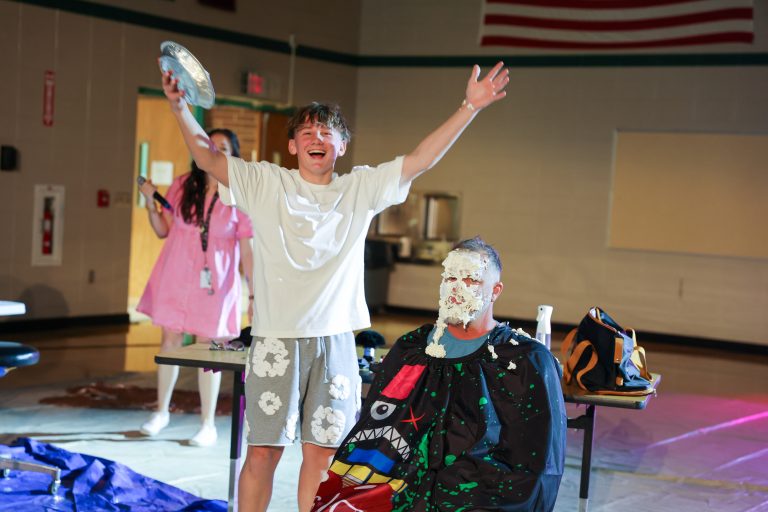 In a school gymnasium, a group of people are celebrating an event, with one person holding a trophy and another wearing a