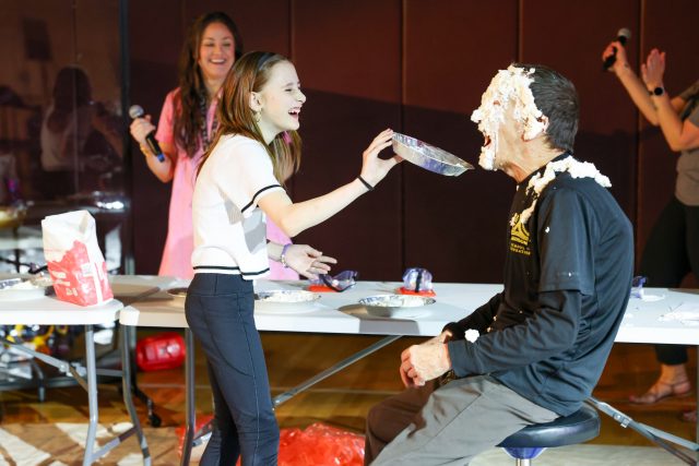 Woman in white shirt holding whipped cream over man's head.