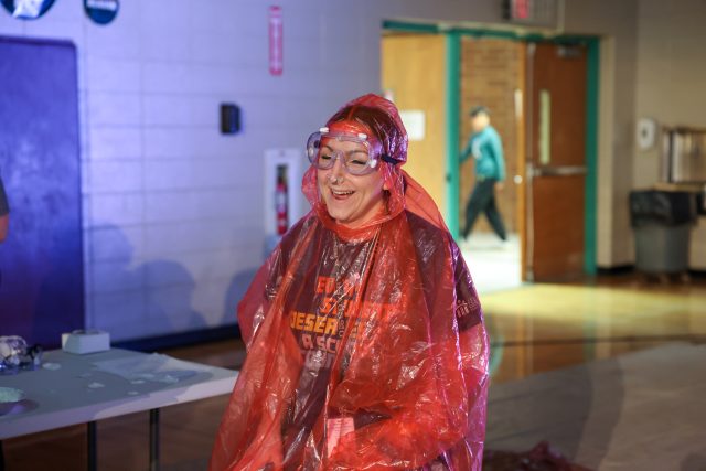 Woman in a red rain poncho standing at a table.