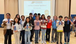 Students holding ribbons in front of a podium at an event.